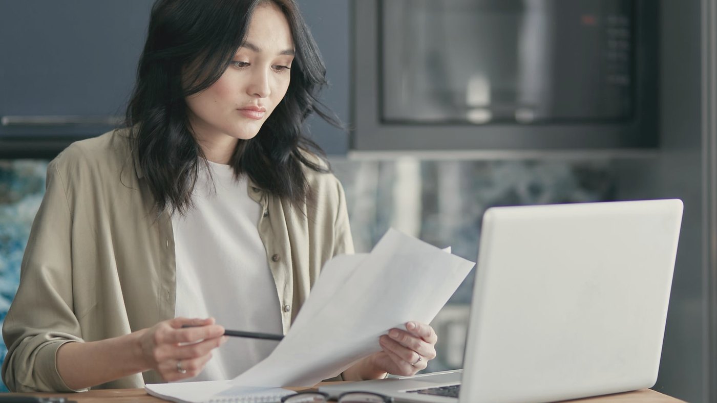 Woman reviewing printed documents while working on a laptop