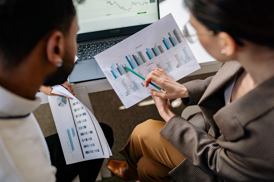Colleagues discussing data charts on printouts at an office desk