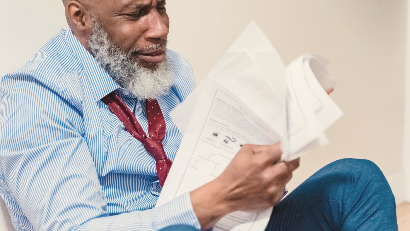 Man in distress sitting against a wall with paperwork around him