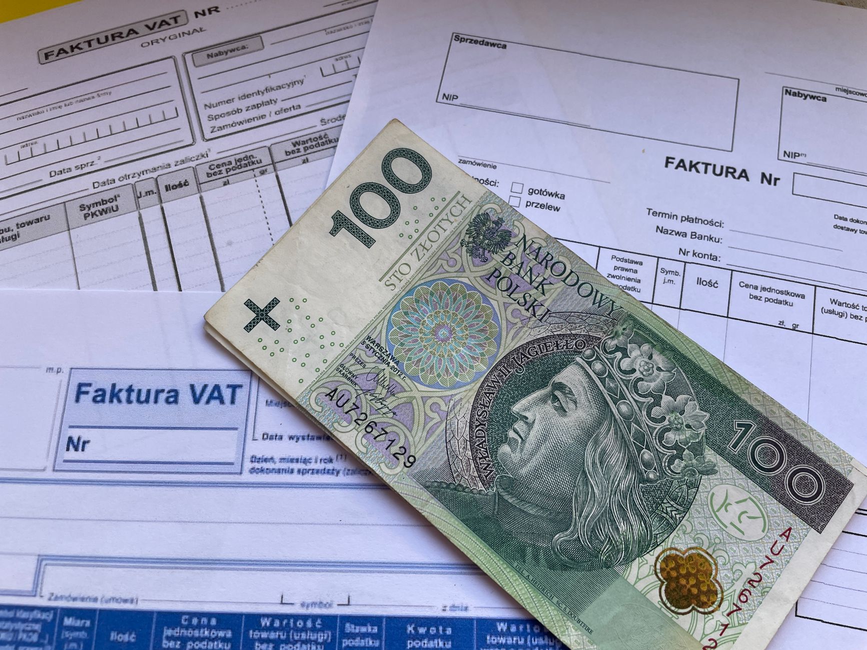 A hundred zloty banknote lies on a stack of VAT invoices