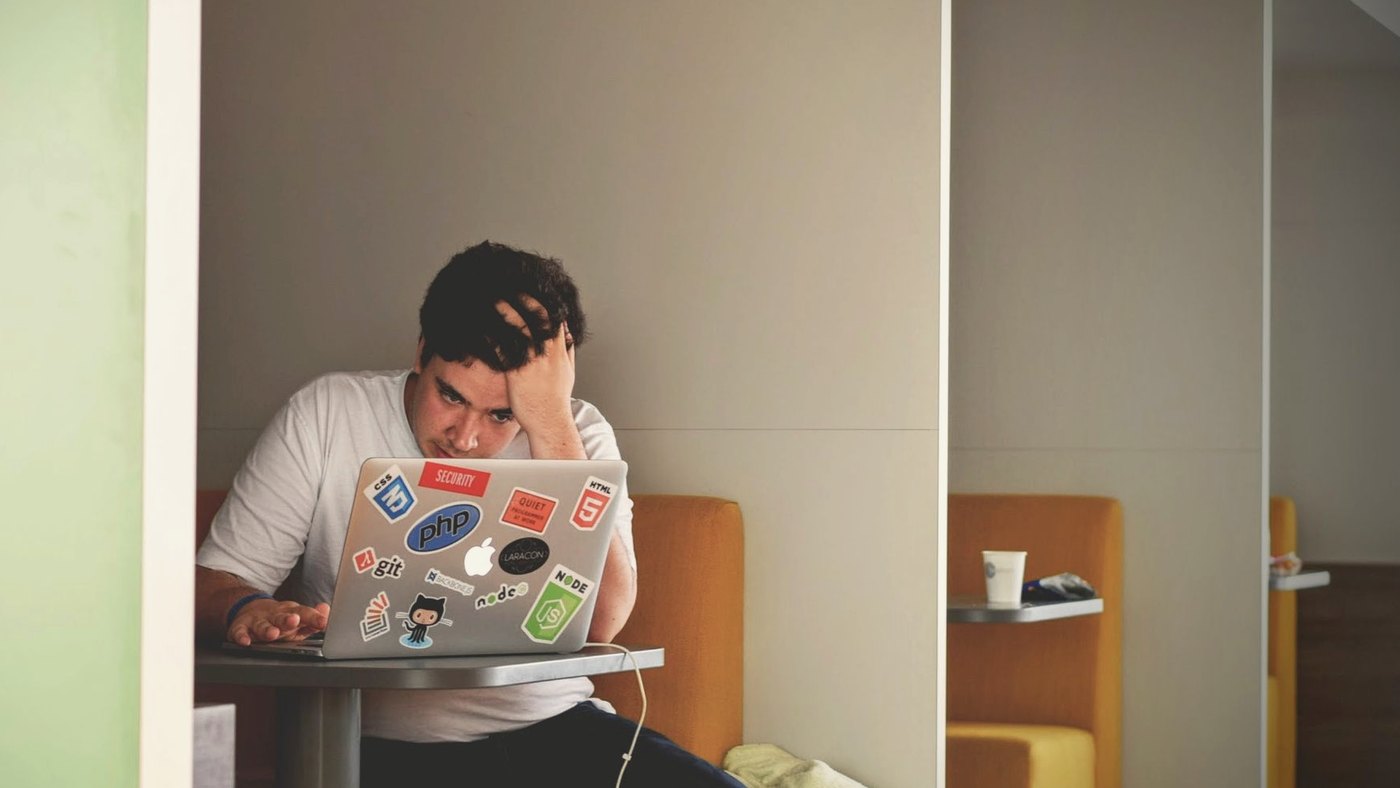 Man in a white shirt gripping his head over a laptop