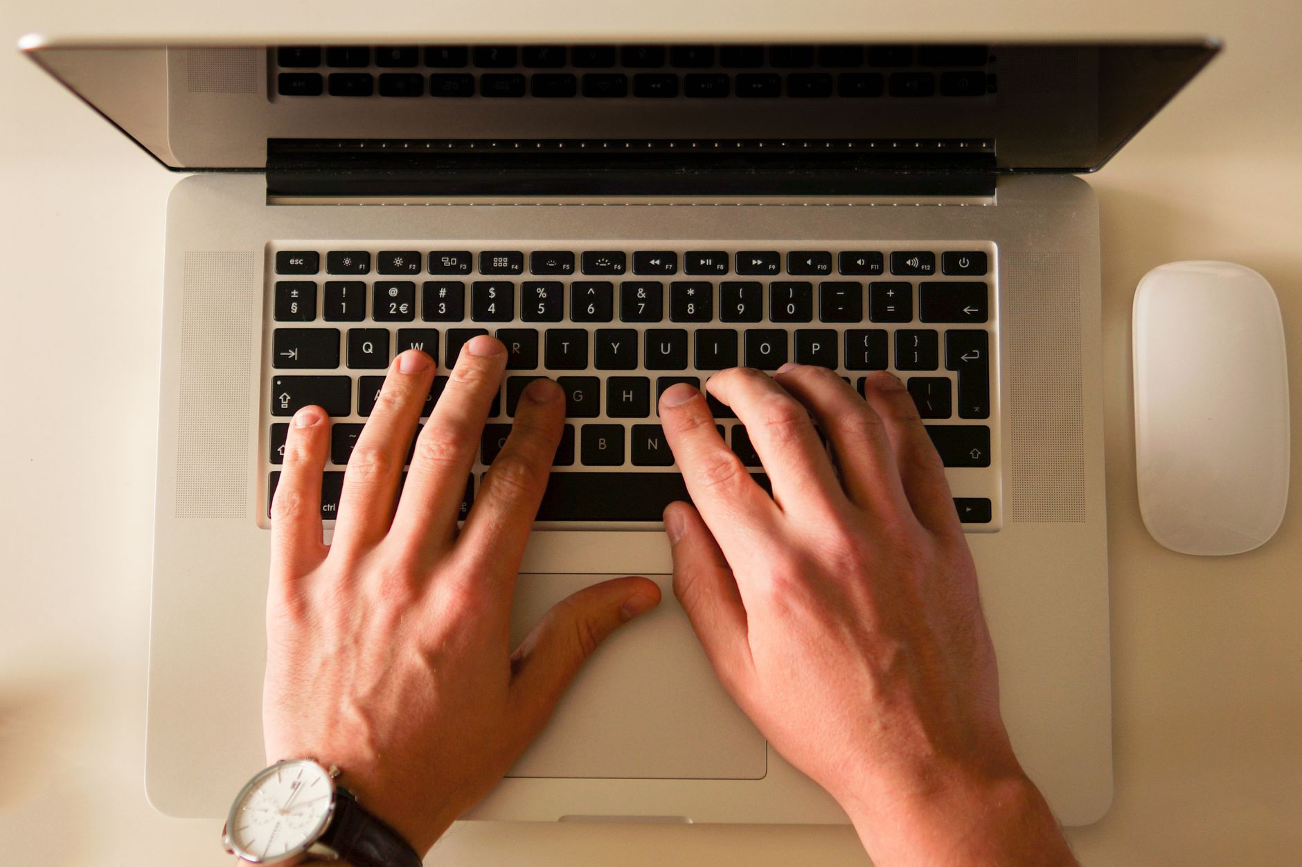 Two hands type on a laptop keyboard next to a mouse