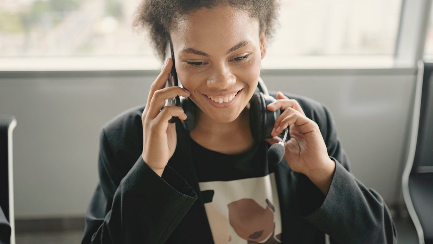 Smiling woman in a headset talks on a phone at her desk