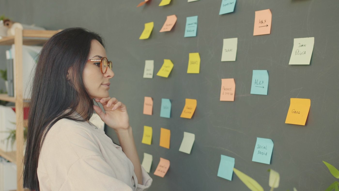 Woman studying colorful sticky notes arranged on a chalkboard