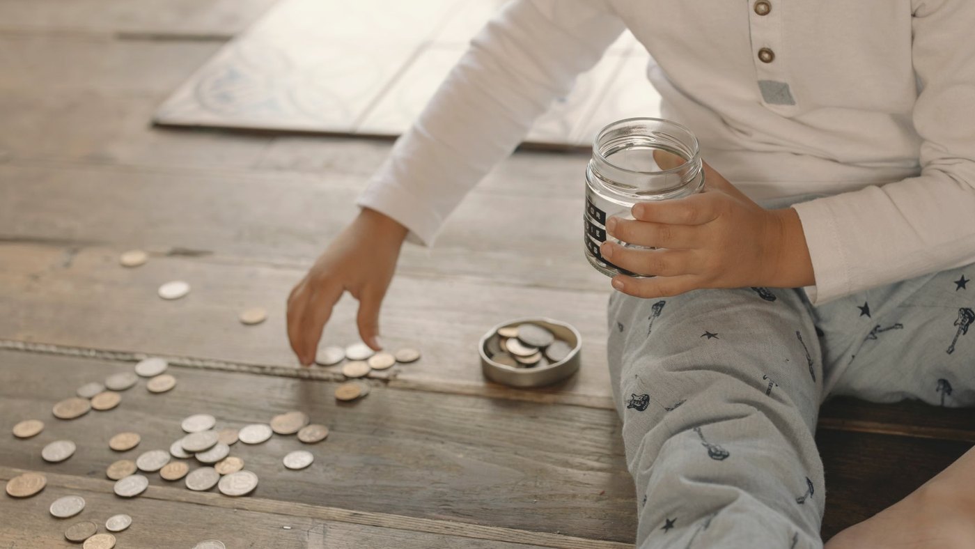 Young child dropping coins into a glass jar