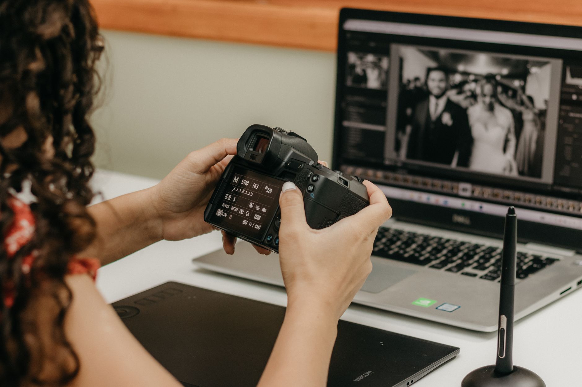 Женщина держит фотокамеру у ноутбука с открытым фоторедактором и графическим планшетом